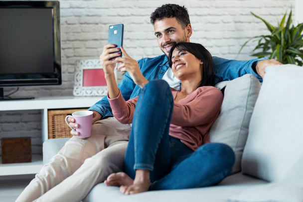 Shot of happy young couple making a video call with smart phone while sitting on couch at home. - Foto, imagen