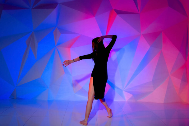 Woman dancing on the background of a beautiful multicolored wall. Sexy slim lonely girl with long black hair in a beautiful dark blue dress. female holds her head. bright colorful geometry backgroun - Foto, afbeelding