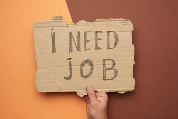 egy darab papír, amire az van írva, hogy munkára van szükségem, a munkanélküliség fogalmára a globális válság közepette, kirúgott alkalmazott, barna háttérrel.  - Fotó, kép