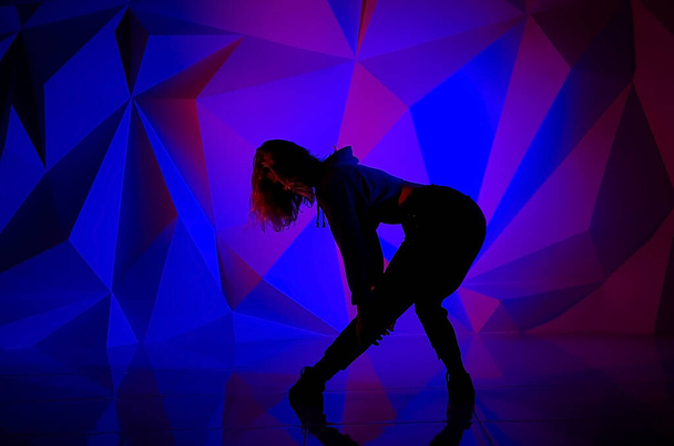 Жінка танцює на тлі красивої різнокольорової стіни. Сексуальна струнка самотня дівчина з довгим чорним волоссям. жінка тримає голову. яскравий барвистий геометричний фон
 - Фото, зображення