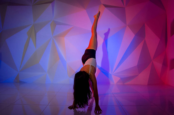 Woman dancing on the background of a beautiful multicolored wall. Sexy slim lonely girl with long black hair. female holds her head. bright colorful geometry backgroun - Photo, Image