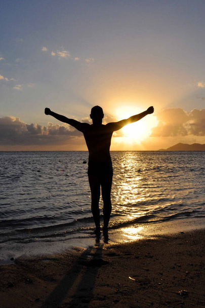 Sziluett a férfi a karok egy kereszt a strandon naplementekor - Fotó, kép