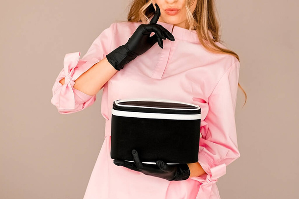 дівчина в рожевому костюмі тримає чорну косметичну сумку. одяг для косметолога, візажиста. Шаблон для реклами
 - Фото, зображення