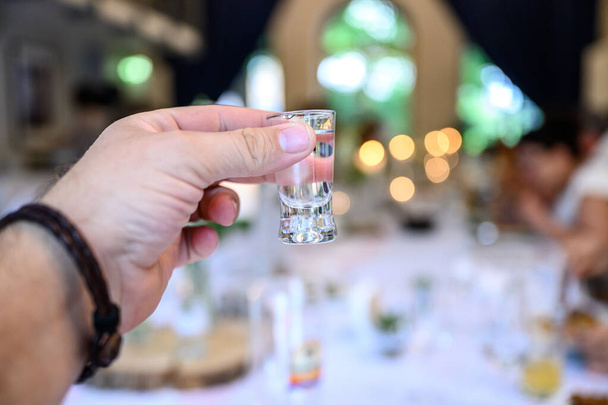 Wedding or party concept. Hand with a glass of vodka guest makes a toast, raising a glass - 写真・画像