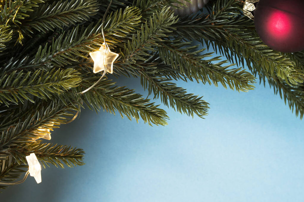 Christmas tree branch with balls and lights closeup on blue background - Φωτογραφία, εικόνα