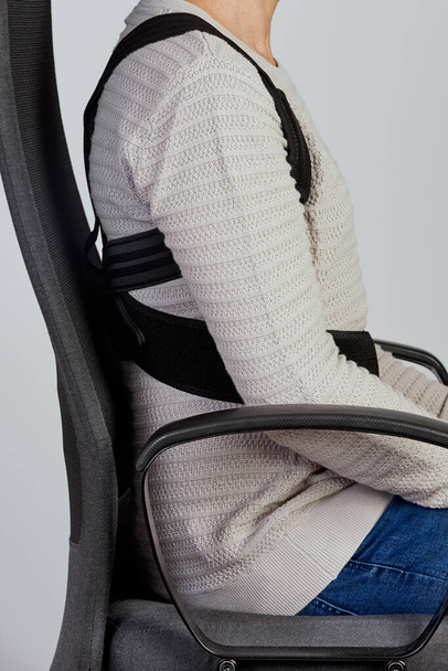 primer plano de un joven caucásico con un corrector de postura en la parte superior de la espalda como está sentado en su silla de oficina - Foto, imagen