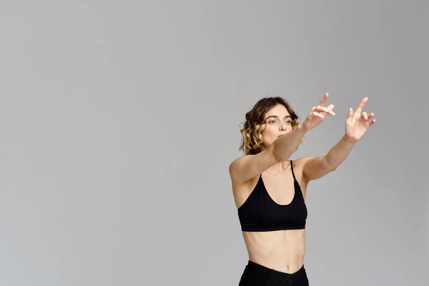 A slender woman in black leggings on a gray background gestures with her hands gymnastics sports - Foto, afbeelding