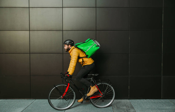 Food delivery rider on his bicycle. Image of a middle age man at work in the city center. Delivering pizza and burgers at home with the thermal backpack - Фото, зображення