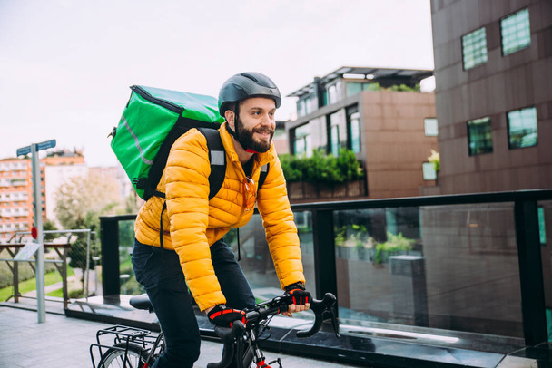 Food delivery rider on his bicycle. Image of a middle age man at work in the city center. Delivering pizza and burgers at home with the thermal backpack - Foto, Imagem