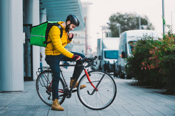 Food delivery rider on his bicycle. Image of a middle age man at work in the city center. Delivering pizza and burgers at home with the thermal backpack - Fotoğraf, Görsel