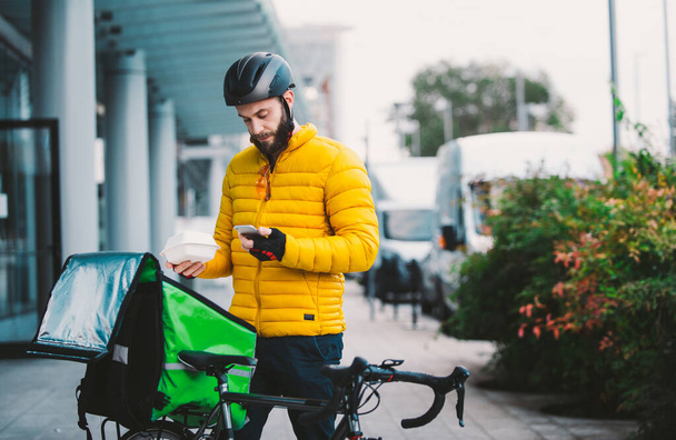 Food delivery rider on his bicycle. Image of a middle age man at work in the city center. Delivering pizza and burgers at home with the thermal backpack - Fotografie, Obrázek