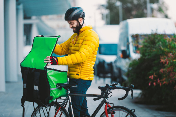 Food delivery rider on his bicycle. Image of a middle age man at work in the city center. Delivering pizza and burgers at home with the thermal backpack - Fotografie, Obrázek