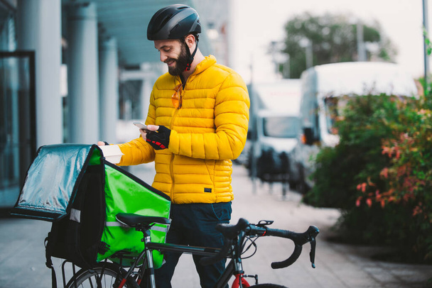 Food delivery rider on his bicycle. Image of a middle age man at work in the city center. Delivering pizza and burgers at home with the thermal backpack - 写真・画像