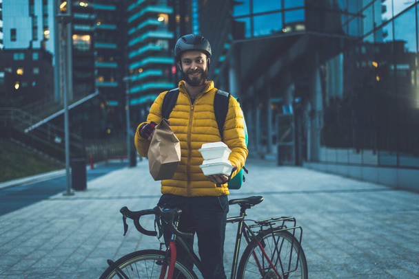 Food delivery rider on his bicycle. Image of a middle age man at work in the city center. Delivering pizza and burgers at home with the thermal backpack - Фото, зображення