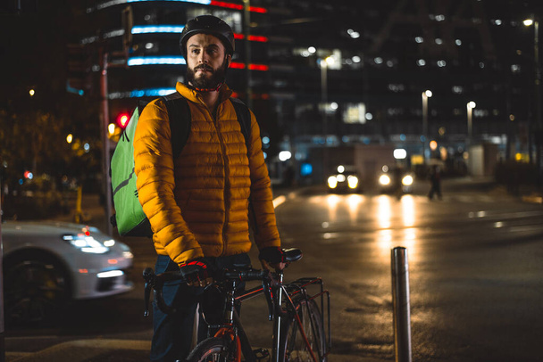 Food delivery rider on his bicycle. Image of a middle age man at work in the city center. Delivering pizza and burgers at home with the thermal backpack - 写真・画像