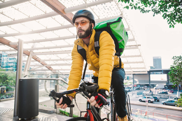 Food delivery rider on his bicycle. Image of a middle age man at work in the city center. Delivering pizza and burgers at home with the thermal backpack - Фото, изображение