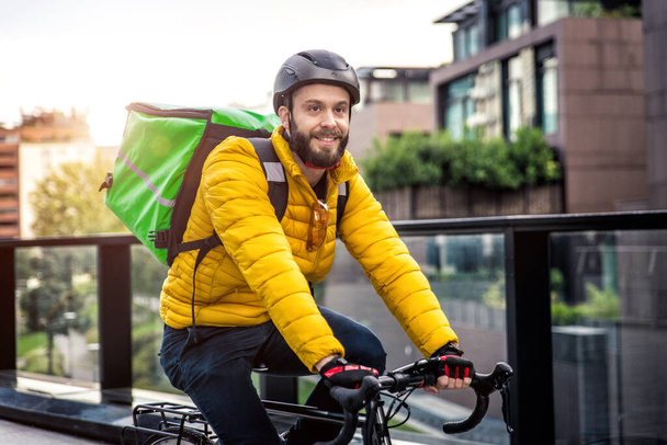 Food delivery rider on his bicycle. Image of a middle age man at work in the city center. Delivering pizza and burgers at home with the thermal backpack - Foto, Imagem