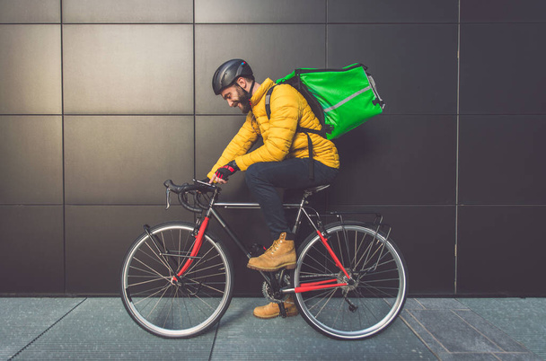Food delivery rider on his bicycle. Image of a middle age man at work in the city center. Delivering pizza and burgers at home with the thermal backpack - Foto, Bild