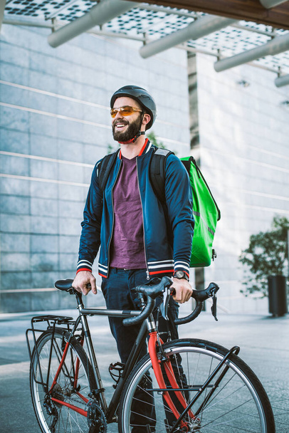 Food delivery rider on his bicycle. Image of a middle age man at work in the city center. Delivering pizza and burgers at home with the thermal backpack - Foto, Imagen