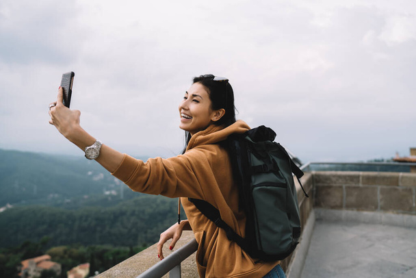 Cheerful asian hipster girl recreating on vacations posing for selfie on destination using smartphone camera, smile woman tourist making pikachu on mobile phone exploring historical places in trip - Fotó, kép