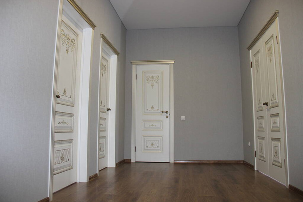 Вид на зал с четырьмя белыми дверями в классическом стиле с золотой патиной, деревянным ламинированным полом, красивыми обоями на стенах - Фото, изображение