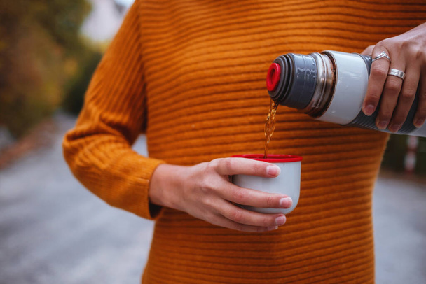 A young tourist woman drinks a hot drink from a cup and enjoys the scenery in the mountains. Trekking concept, Warm autumn weather, calm scene. Wanderlust photo series. - Foto, imagen