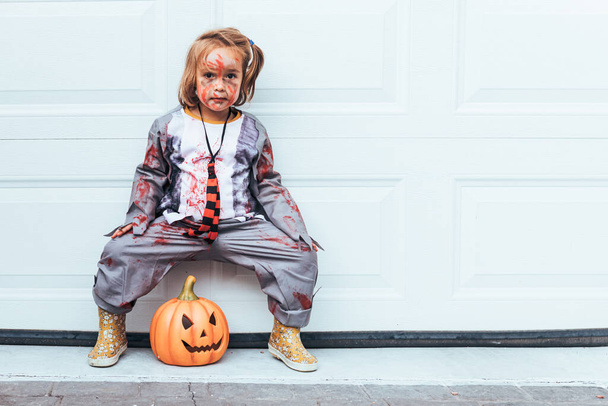 Girl dressed as zombie celebrating Halloween at the garage door next to Jack O Lantern - Photo, Image