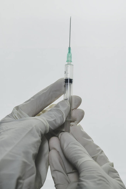 Les mains en gants de latex blanc tiennent une seringue hypodermique sur fond blanc Conceptuel de la médecine, vaccination, covide-19, sars-cov-2 - Photo, image