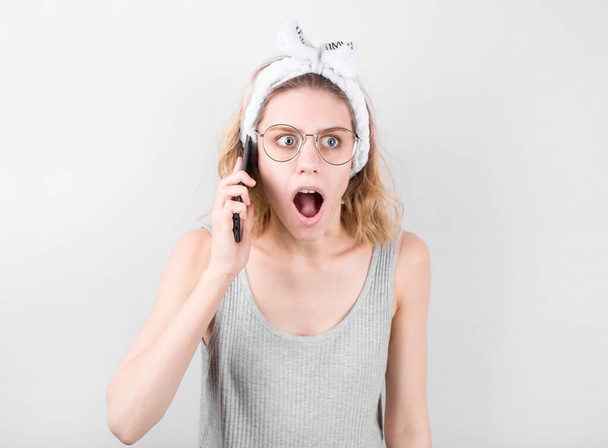 Portrait of a shocked young casual blonde woman talking on mobile phone isolated over white background. - Zdjęcie, obraz