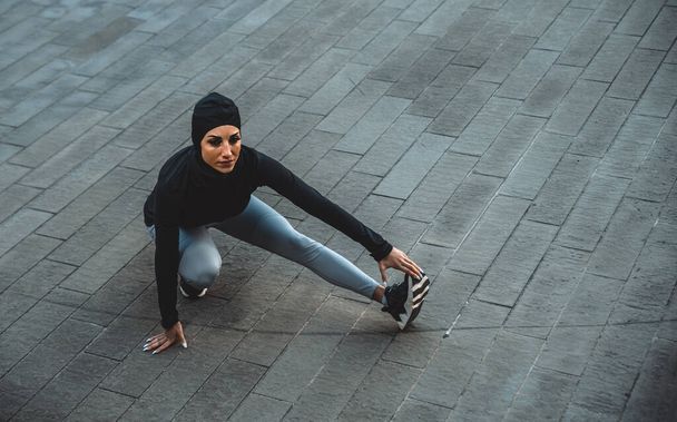 Мусульманский бегун тренируется в центре города. Женщина занимается спортом ранним утром - Фото, изображение