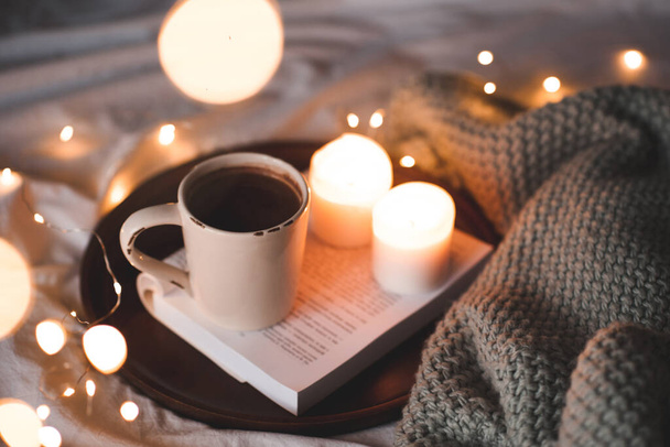 Egy csésze forró csokoládé égő gyertyákkal és kötött textilrel az ágyban, közelről. Éjszaka van. Téli ünnepek.  - Fotó, kép