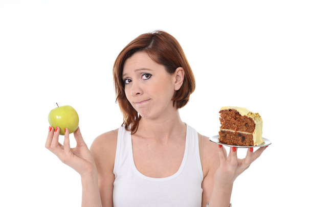 junge attraktive Sport rote Haare Frau mit Apfel und Kuchen in den Händen in gesunden versus Junk Food Dessert Wahl isoliert auf weißem Hintergrund - Foto, Bild