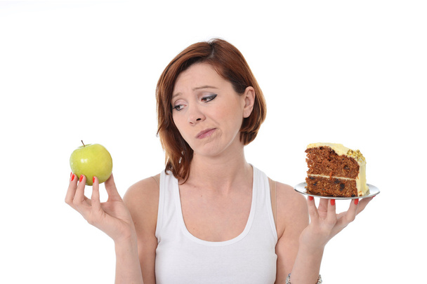 Nuori houkutteleva urheilu punaiset hiukset Nainen, jolla on omena ja kakku käsissä terveellisessä vs roskaruoka jälkiruoka valinta eristetty valkoisella taustalla
 - Valokuva, kuva