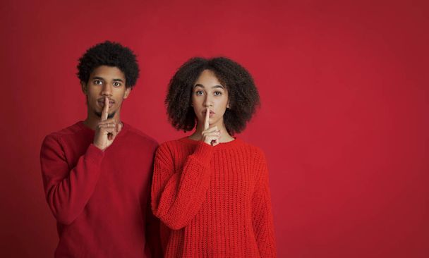 Ruhige afrikanisch-amerikanische junge Frau und Mann in Pullovern machen Schweigezeichen, halten die Vorderfinger auf den Lippen - Foto, Bild