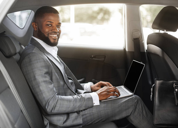 Smiling black guy businessman working on laptop with blank screen - Photo, Image