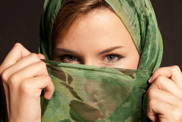 Young arab woman with veil showing her eyes on dark gray background - Foto, imagen