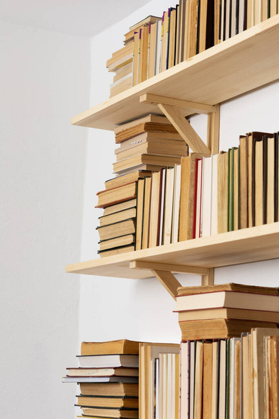 Librerie in legno chiaro con libri rigidi rovesciati in interni bianchi, biblioteca domestica - Foto, immagini