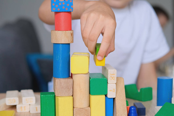kid, boy builds towers and buildings from colored wooden figures, concept of housing construction, mortgage, insurance, happy childhood, children's games - Foto, Bild