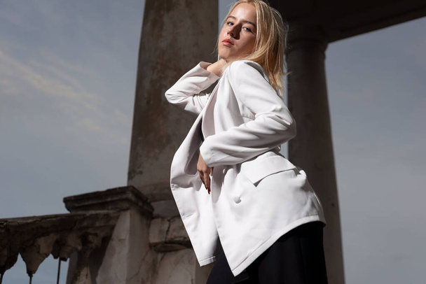 retrato de una modelo rubia, chica de moda en una chaqueta blanca, posando, sobre el fondo de columnas vintage. belleza y moda de las jóvenes adolescentes, generación Y. - Foto, imagen