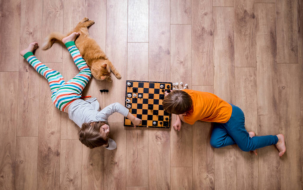 Niños jugando al ajedrez tirados en el suelo y pensando intensamente. Juegos Hermano y hermana y su gato mascota jugando a la mesa juego. - Foto, Imagen