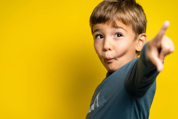 Portret van gelukkige kleine blanke jongen voor gele achtergrond wijzende vinger - Jeugd opgroeien en prestatie concept - vooraanzicht taille omhoog kopieerruimte - Foto, afbeelding