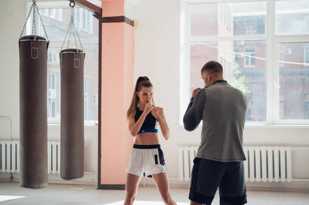 Kickbox 'ta acemi bir kız dövüşçünün ilk eğitimi, koç yumrukları gösteriyor. - Fotoğraf, Görsel