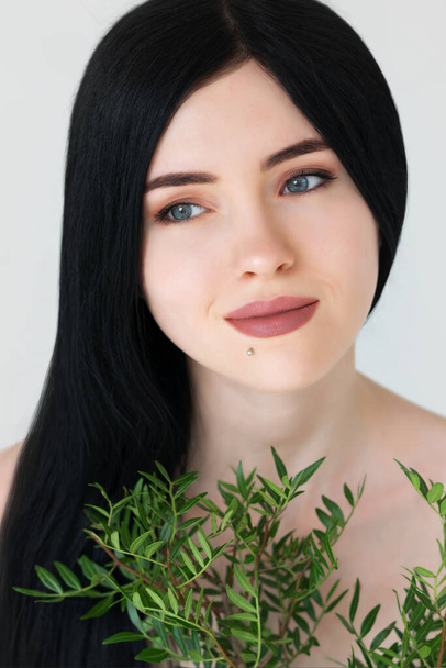 Portrait of beautiful womans face with bouquets of green foliage over light gray background. - Foto, immagini