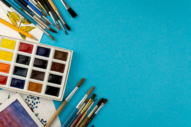 Watercolor paints and brushes. Artists workplace and desk. Color palette. Drawing blue background. Place for your text. Art created. Copy space. - Φωτογραφία, εικόνα