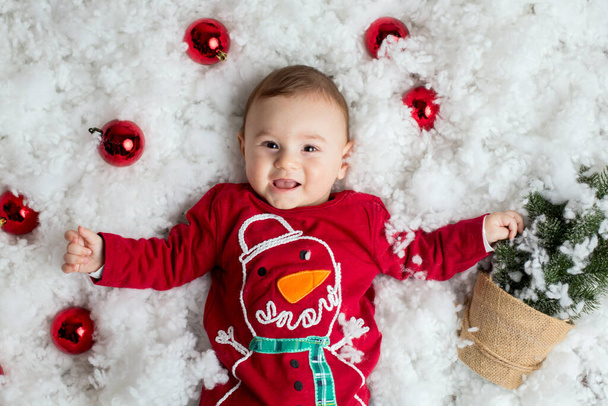 Милый маленький мальчик с рождественскими украшениями, играющий в снегу - Фото, изображение