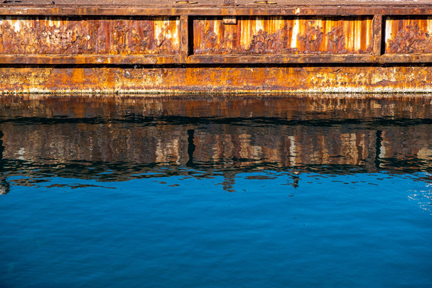 Paslı metal eski endüstriyel liman rıhtımı berrak mavi deniz suyuna yansıyor. - Fotoğraf, Görsel