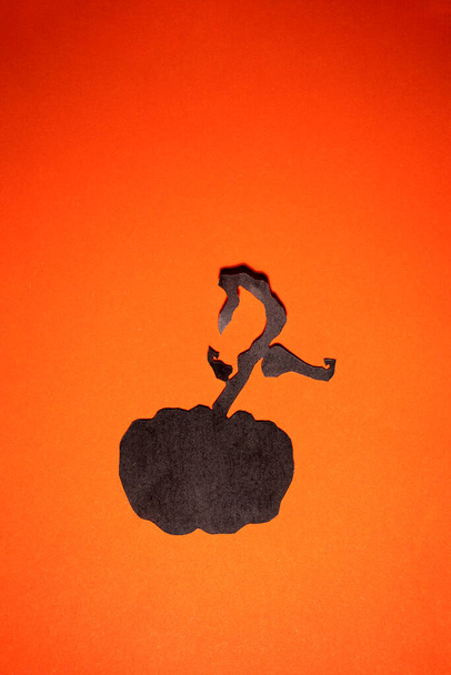 Schwarz gefärbter ausgeschnittener handwerklicher Kürbis auf orangefarbenem Hintergrund - Foto, Bild