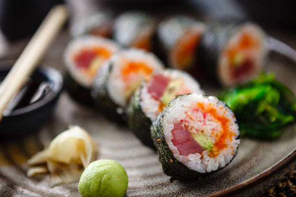 Rollos de maki de sushi con atún, caviar de pescado volador, cangrejo, aguacate en un plato con palillos, salsa de soja, wasabi y jengibre. Primer plano de la comida tradicional japonesa servida para el almuerzo en el restaurante gourmet moderno. - Foto, imagen