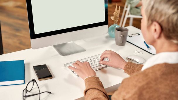 Eine weiße reife, gut gekleidete Damenchefin mit Kurzhaarschnitt sitzt an einem Tisch und arbeitet an ihrem PC - Foto, Bild