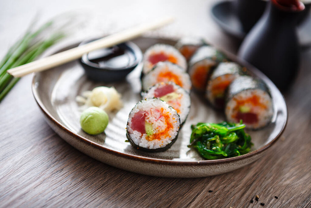 Rouleaux de maki sushi au thon, caviar de poisson volant, crabe, avocat dans une assiette avec baguettes, sauce soja, wasabi et gingembre. Nourriture traditionnelle japonaise servie en gros plan pour le déjeuner dans un restaurant gastronomique moderne. - Photo, image